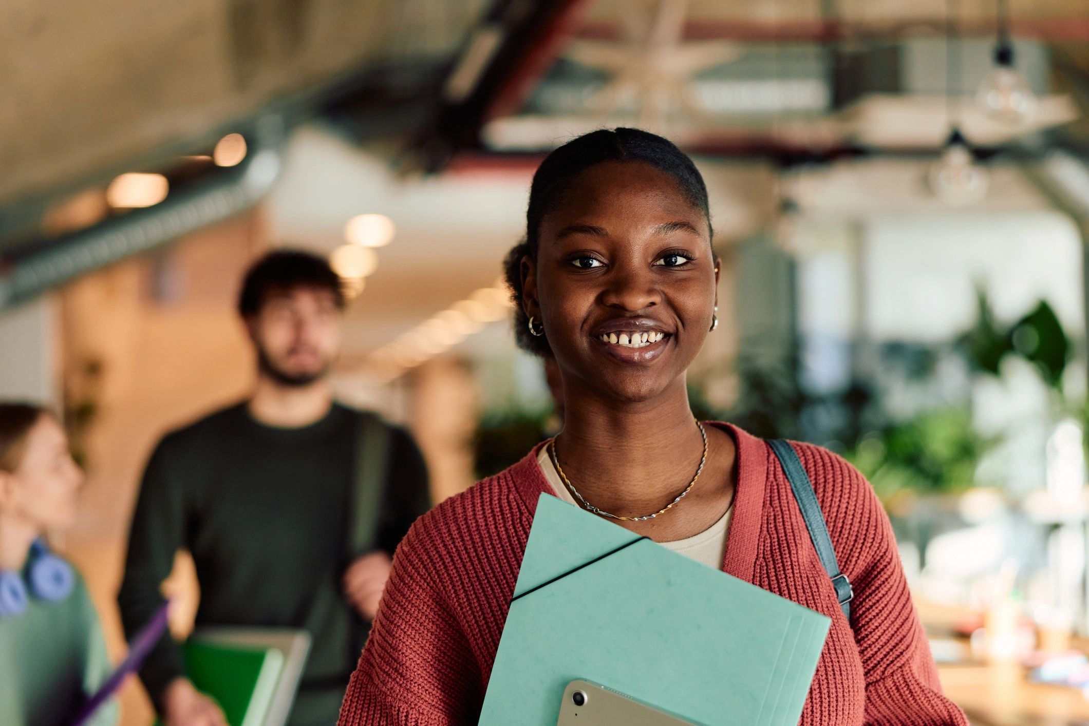 Black student holding a folder and tablet in a university hallway